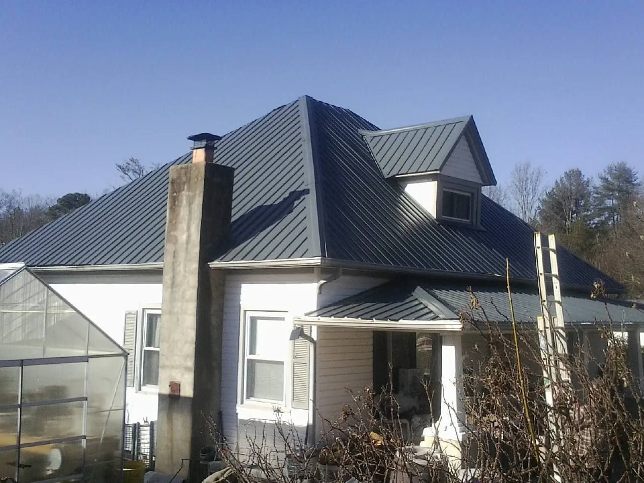 Dark blue standing seam metal roof on a white farmhouse with dormer — Slate & Tile Roof Repair by Roofing Brothers in Misenheimer
