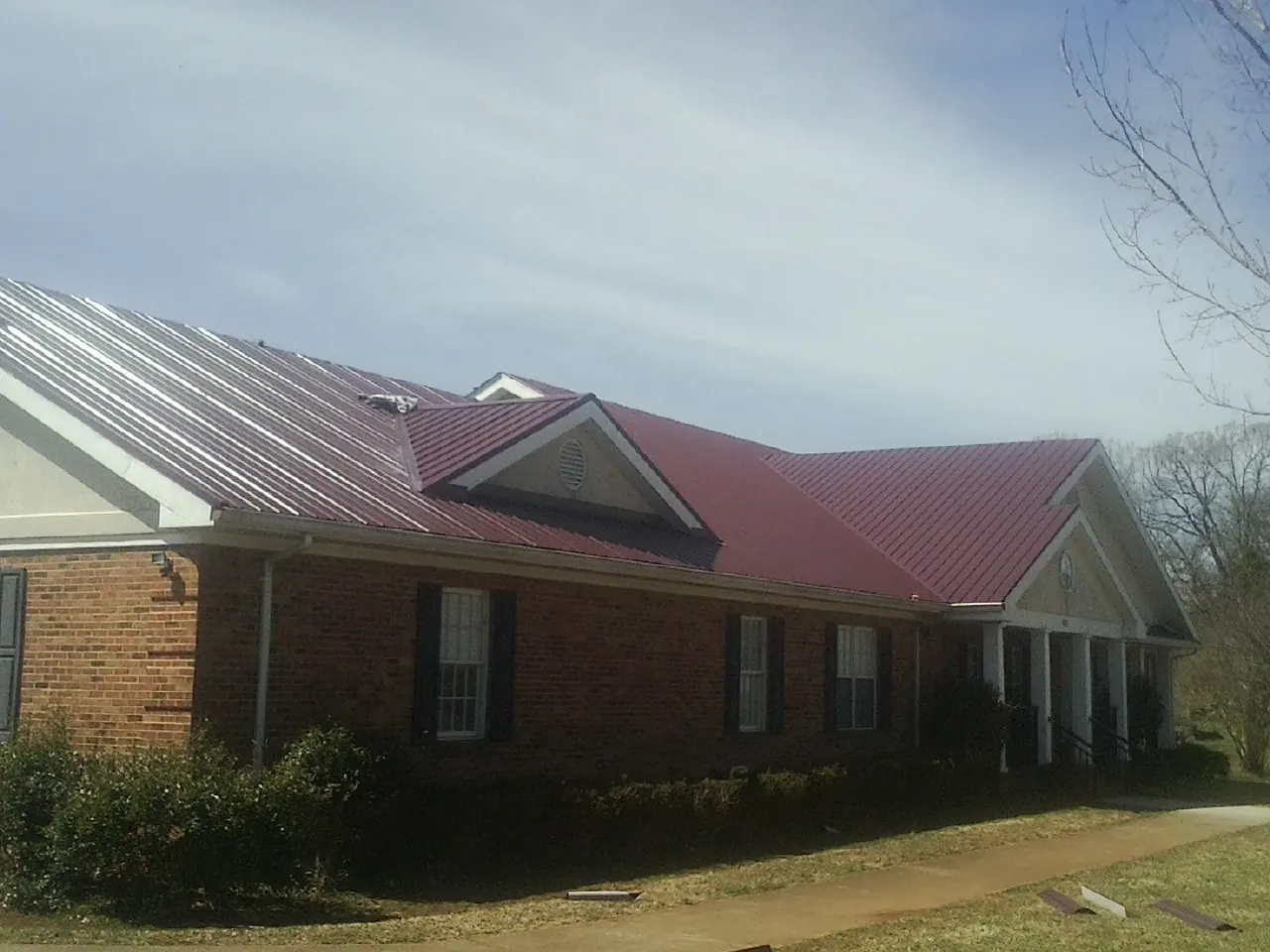 Red metal roof with gabled entries on a long brick building, from a Hail Damage Roof Repair job in Misenheimer