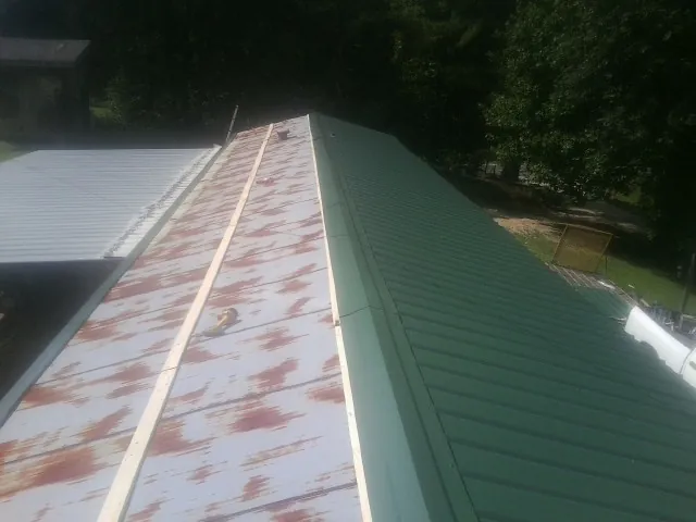 Old rusted panels beside newly installed green metal roofing — Wind Damage Roof Repair by Roofing Brothers in Misenheimer