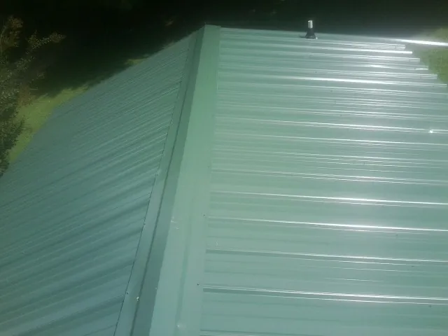 New green metal panels meeting at the ridge of a roof — Flat Roof Repair work by our crew in Misenheimer