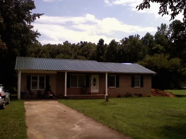 Dark green metal roof on a brick ranch with a covered porch in Misenheimer