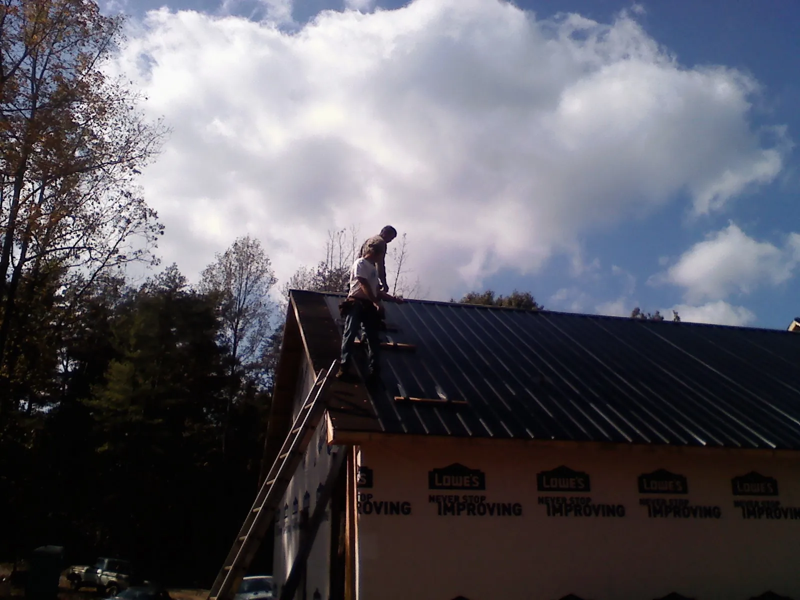 Roofer fastening dark metal panels high against a cloudy sky, from a Roof Inspection job in Misenheimer