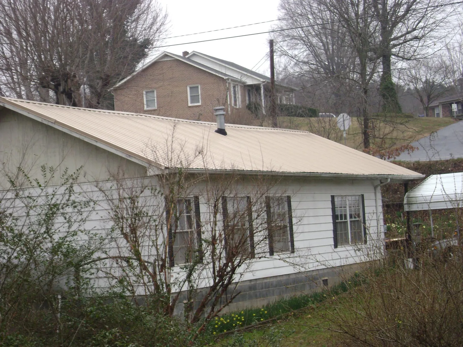 Tan metal roof on a white sided house set into a hillside — Commercial Roofing by Roofing Brothers in Misenheimer