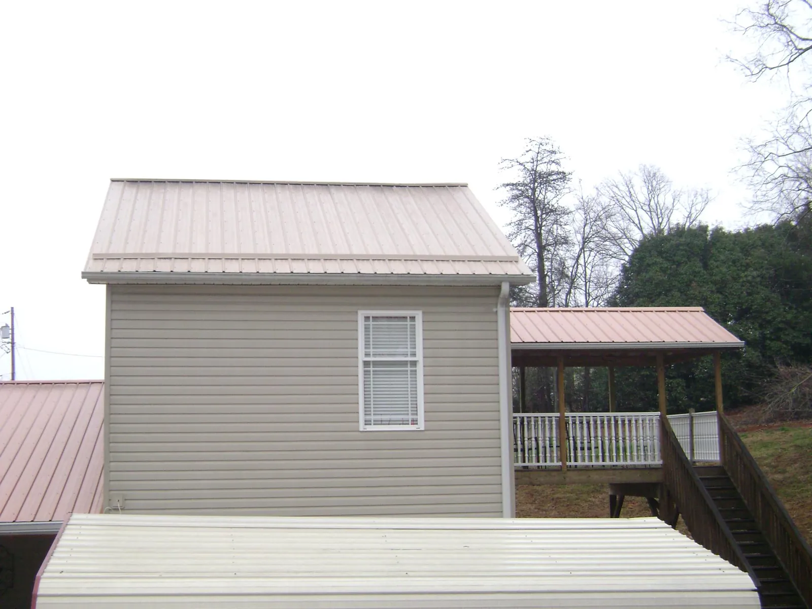 Tan metal roofs on a two story addition and attached porch, from a Roof Replacement job in Misenheimer
